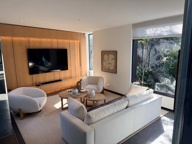 Modern living room featuring high-quality timber wall paneling, integrated cabinetry, recessed lighting, and large windows overlooking a private garden area.