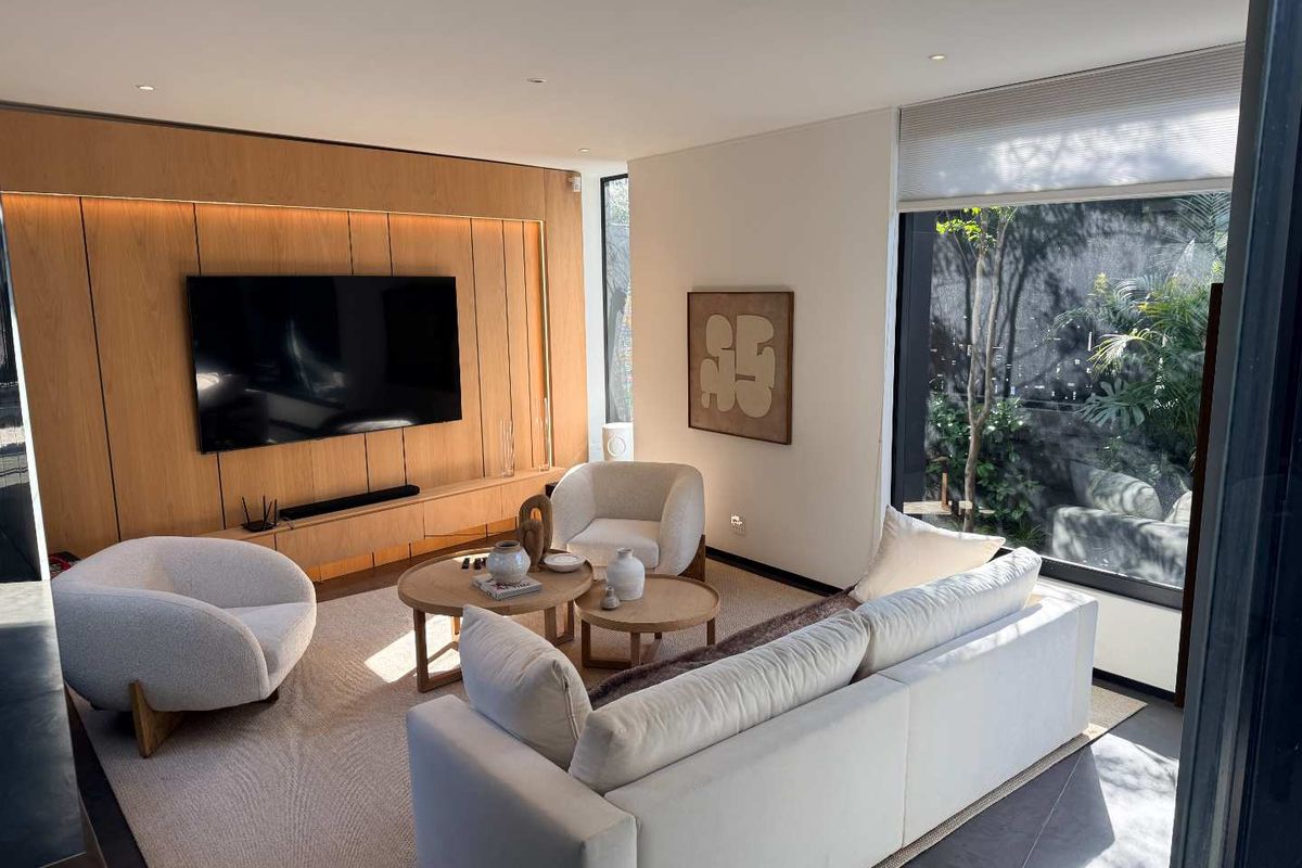 Modern living room featuring high-quality timber wall paneling, integrated cabinetry, recessed lighting, and large windows overlooking a private garden area.