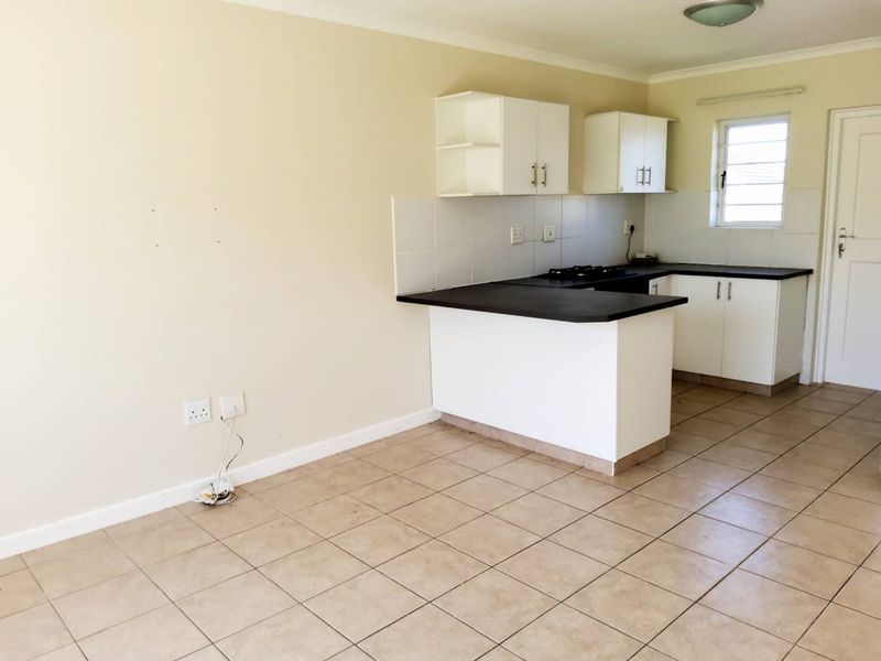 Open plan kitchen area featuring tiled flooring, built-in cabinetry with dark countertops, and a gas hob, presented in a clean, vacant condition.