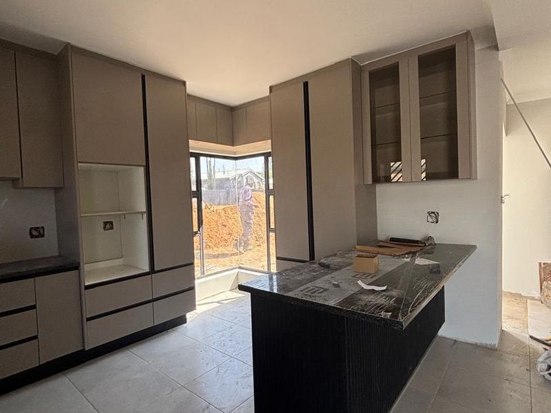Modern kitchen under construction featuring sleek built-in cabinetry, a central island with stone countertops, and large corner windows allowing natural light.