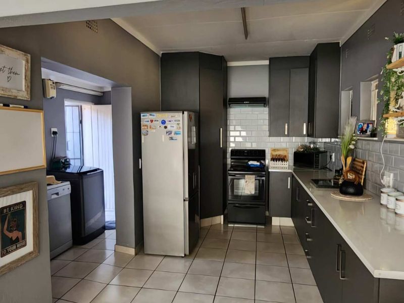 A functional kitchen featuring dark cabinetry, subway tile backsplash, stone countertops, and integrated appliances, with an adjacent utility area.
