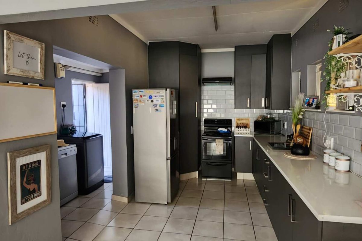 A functional kitchen featuring dark cabinetry, subway tile backsplash, stone countertops, and integrated appliances, with an adjacent utility area.