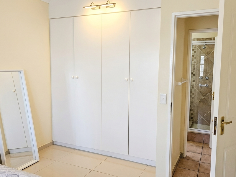 A well-maintained bedroom featuring built-in wardrobes, tiled flooring, and direct access to an en-suite bathroom.