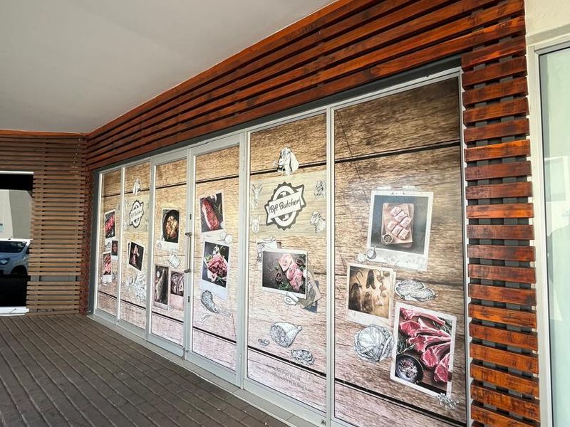 Front facade of a commercial butcher shop featuring timber slat detailing, paved walkway, and large glass storefront with branded window graphics.