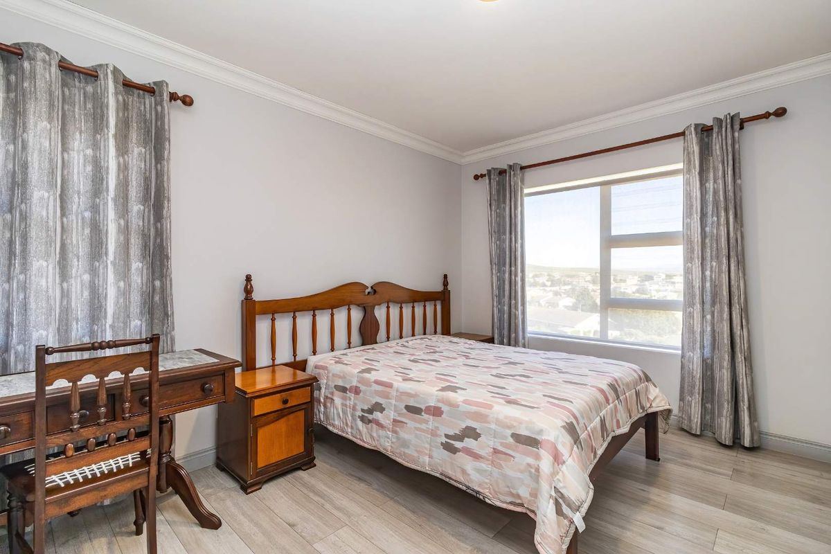 A well-lit bedroom featuring modern laminate flooring, decorative ceiling cornicing, and a large window providing natural light and exterior views.