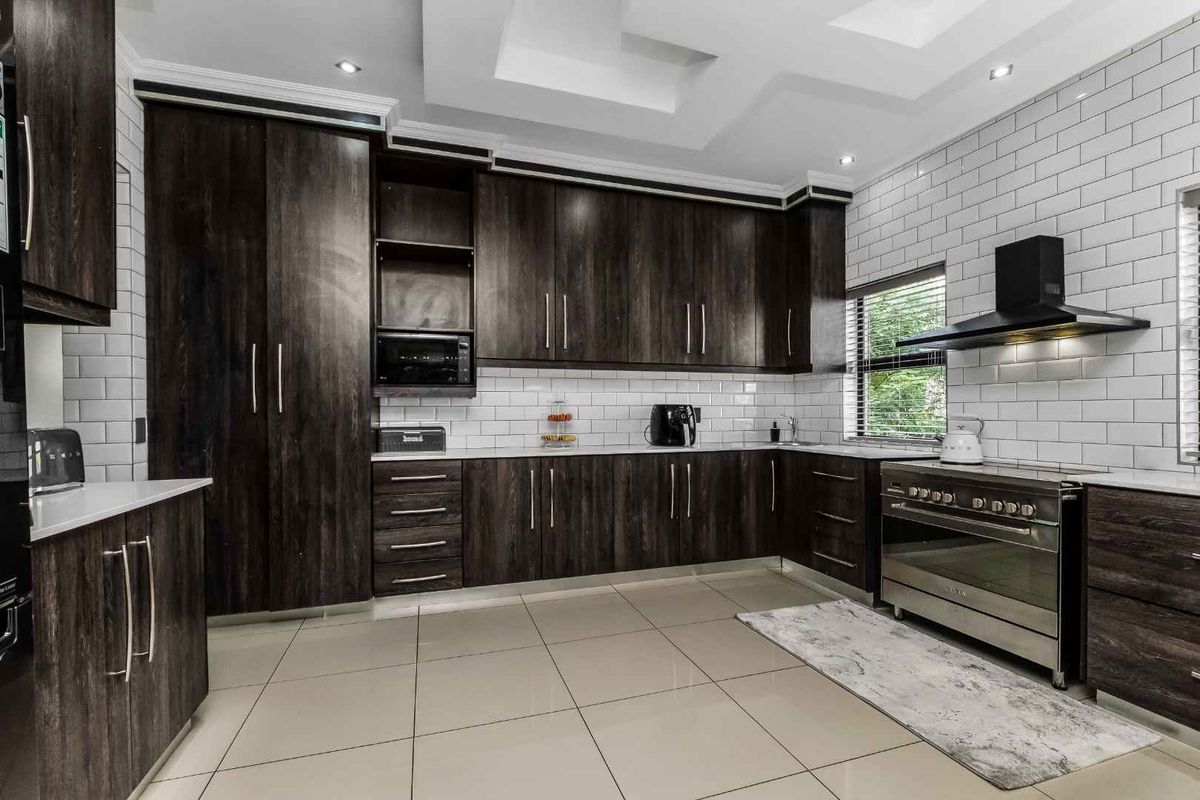 Modern kitchen featuring dark wood cabinetry, white subway tile backsplash, tiled flooring, and a stainless steel freestanding oven with a black extractor fan.