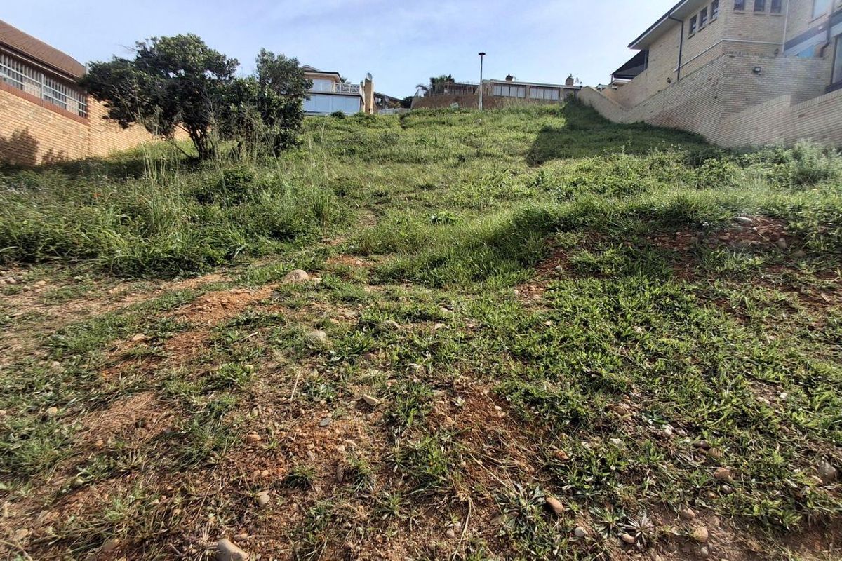 A sloped vacant residential plot featuring established grass cover and bordering brick retaining walls, situated between existing residential properties.