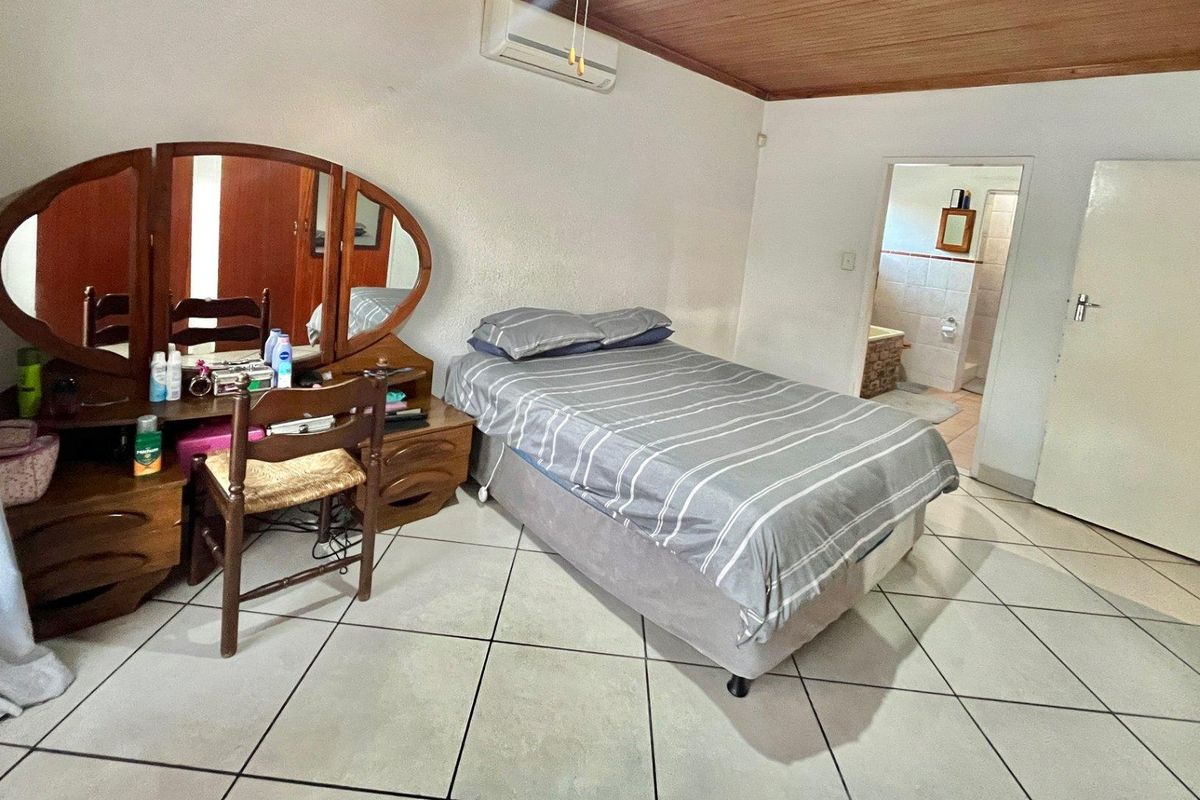 A bedroom featuring tiled flooring, a timber-paneled ceiling, and an integrated air conditioning unit, with an adjoining en-suite bathroom.