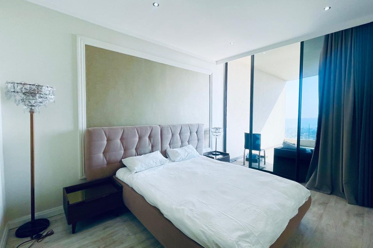 Spacious bedroom featuring floor-to-ceiling glass doors with balcony access, recessed lighting, and elegant wall molding, offering a bright and modern living space.
