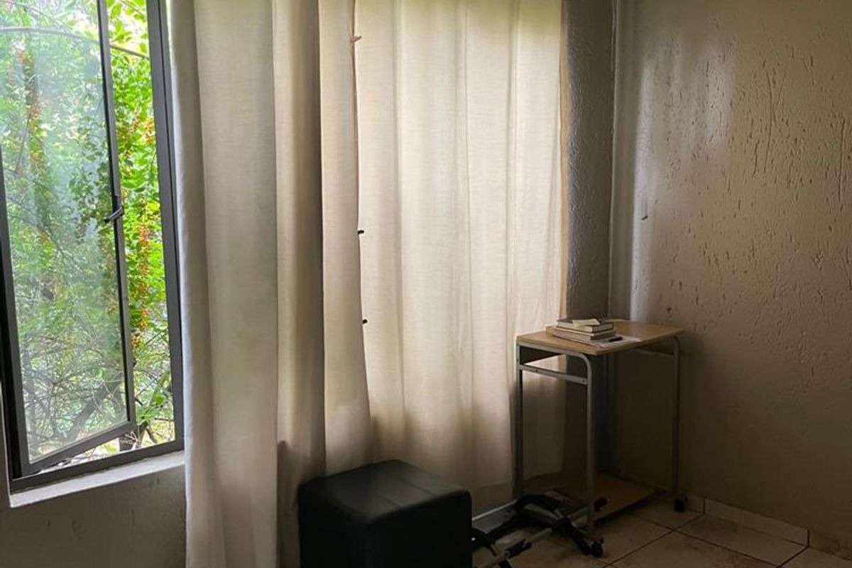 A bedroom featuring tiled flooring and a large casement window with curtain fixtures, requiring cosmetic wall repairs and updates.