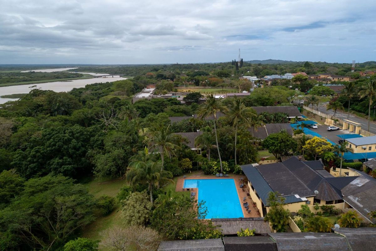 Aerial view of the apartment complex featuring a large communal swimming pool, lush landscaped gardens, and scenic river views.