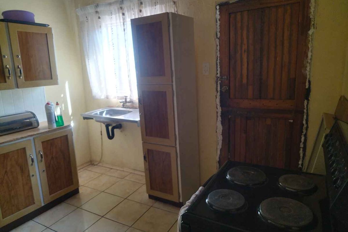 A functional kitchen featuring built-in cabinetry, a stainless steel sink, and tiled flooring, currently requiring cosmetic updates and finishing touches to the door frame.