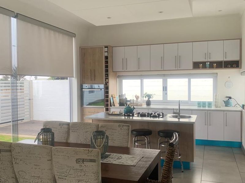 Modern open-plan kitchen and dining area featuring sleek cabinetry, a central island with a gas hob, and large windows with roller blinds.