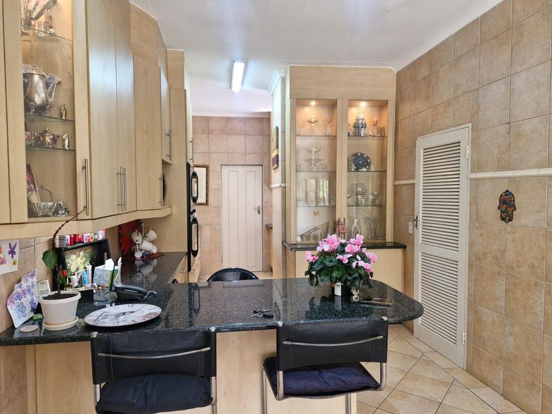 A functional kitchen featuring light wood cabinetry, granite countertops, built-in display units, and tiled finishes throughout.