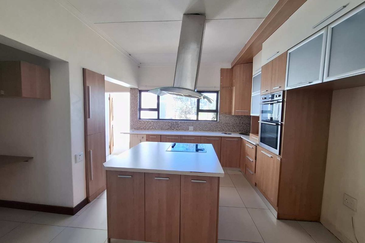A functional kitchen featuring light wood cabinetry, a central island with a built-in hob, stainless steel extractor fan, and integrated double oven.