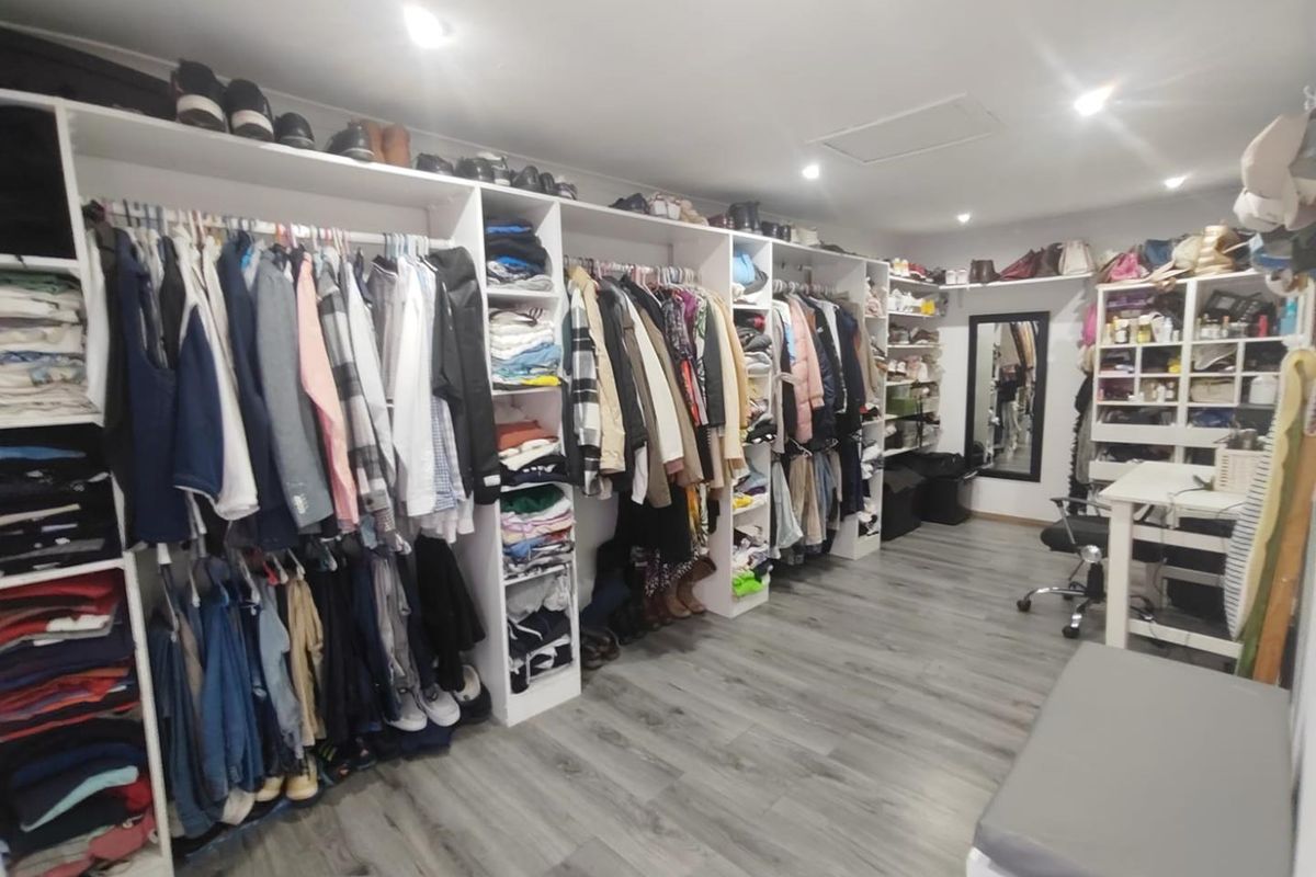 A spacious walk-in wardrobe featuring extensive built-in shelving, hanging rails, and modern laminate flooring with recessed ceiling lighting.