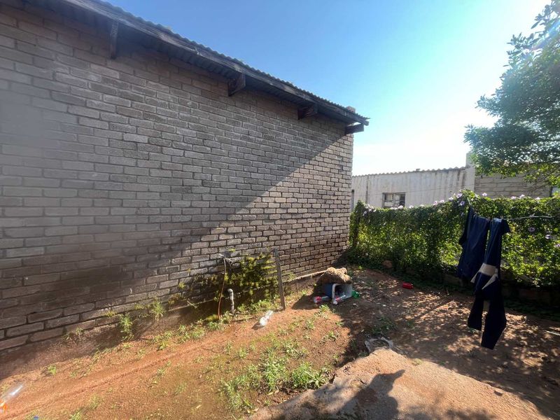 A view of the rear exterior brick wall and corrugated roof, featuring an external water tap and surrounding garden area.