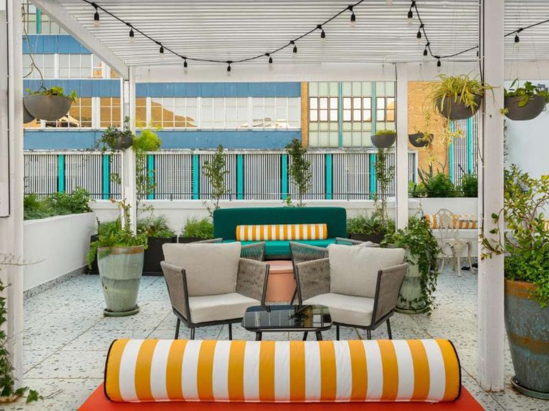 A well-maintained outdoor patio area featuring a white pergola structure, string lighting, and tiled flooring, providing a pleasant space for relaxation.