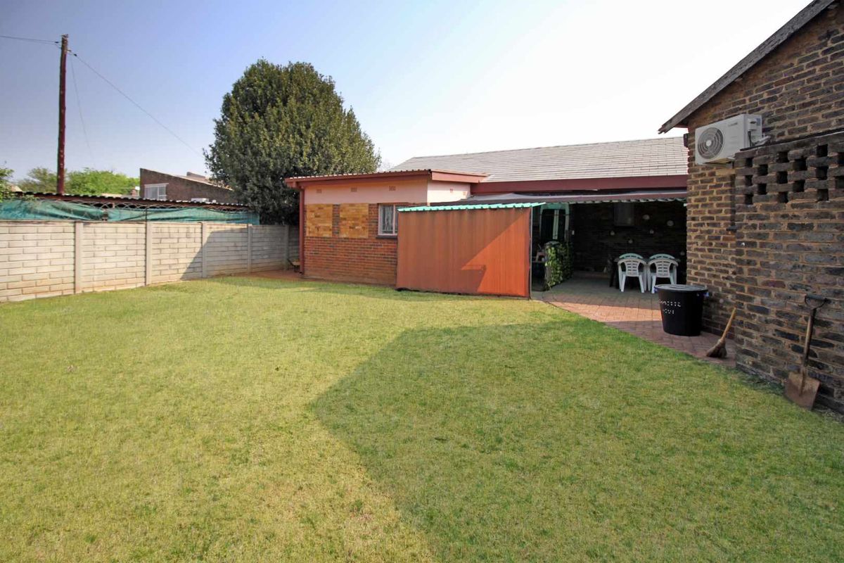 A spacious rear garden featuring a paved patio area, brick boundary walls, and a lawn, providing a functional outdoor space for the property.