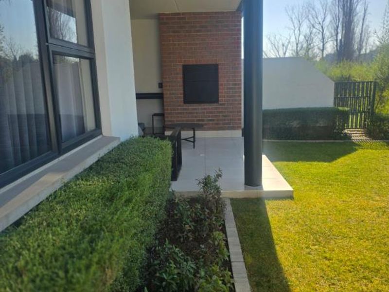 A covered patio area featuring a built-in braai, brick accent wall, and tiled flooring, overlooking a private garden space.