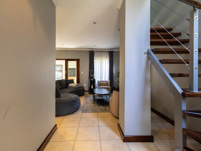 An inviting living area featuring tiled flooring and a modern staircase with timber treads and metal balustrades, leading to an open-plan lounge space.