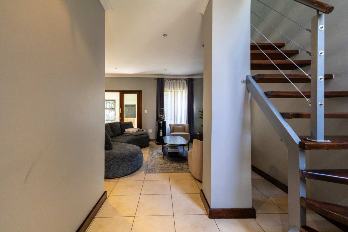 An inviting living area featuring tiled flooring and a modern staircase with timber treads and metal balustrades, leading to an open-plan lounge space.