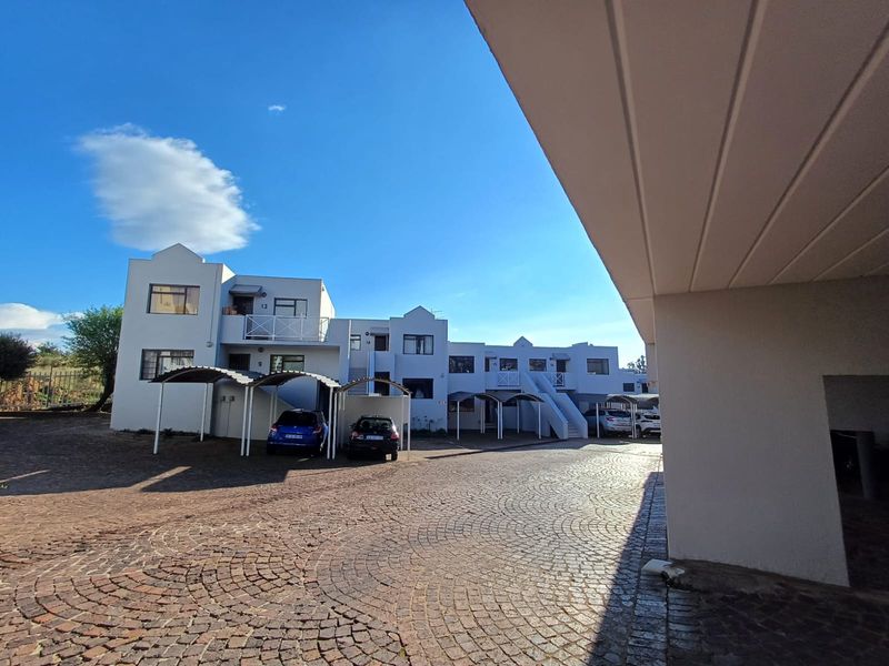 Exterior view of an apartment complex featuring paved driveway, covered parking carports, and multi-level residential units with balconies and external staircases.