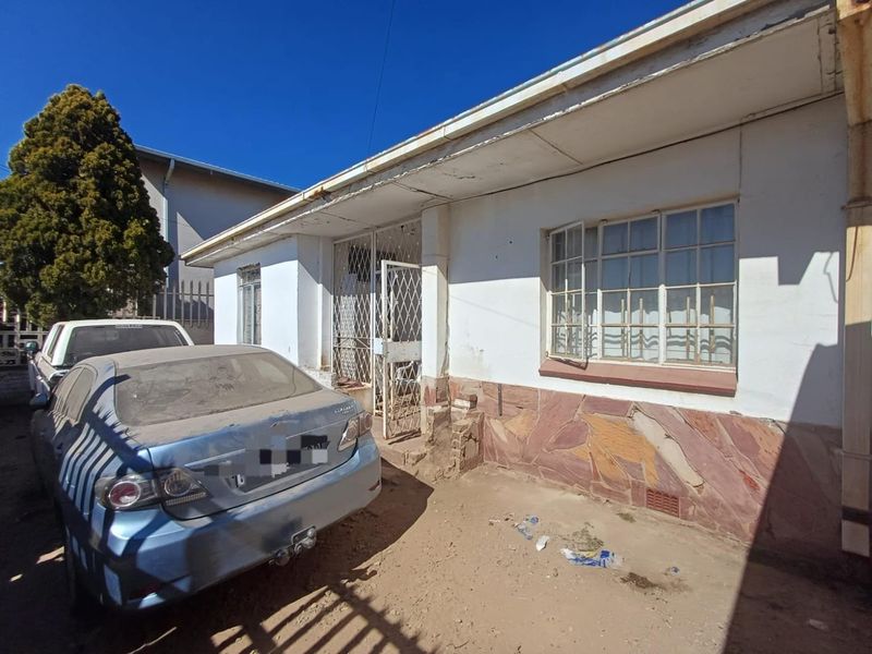 Front exterior view of a house featuring stone cladding, steel window frames, and a security gate, showing signs of significant wear and maintenance needs.