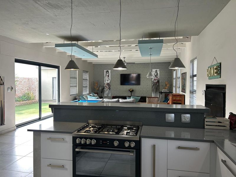 Spacious open-plan living area featuring a modern kitchen with gas stove, stone countertops, and seamless flow to the outdoor garden through sliding glass doors.