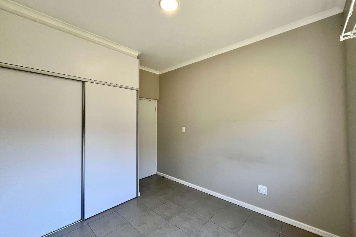 An empty bedroom featuring tiled flooring, a built-in sliding door wardrobe, and neutral wall finishes, providing a clean canvas for personalization.