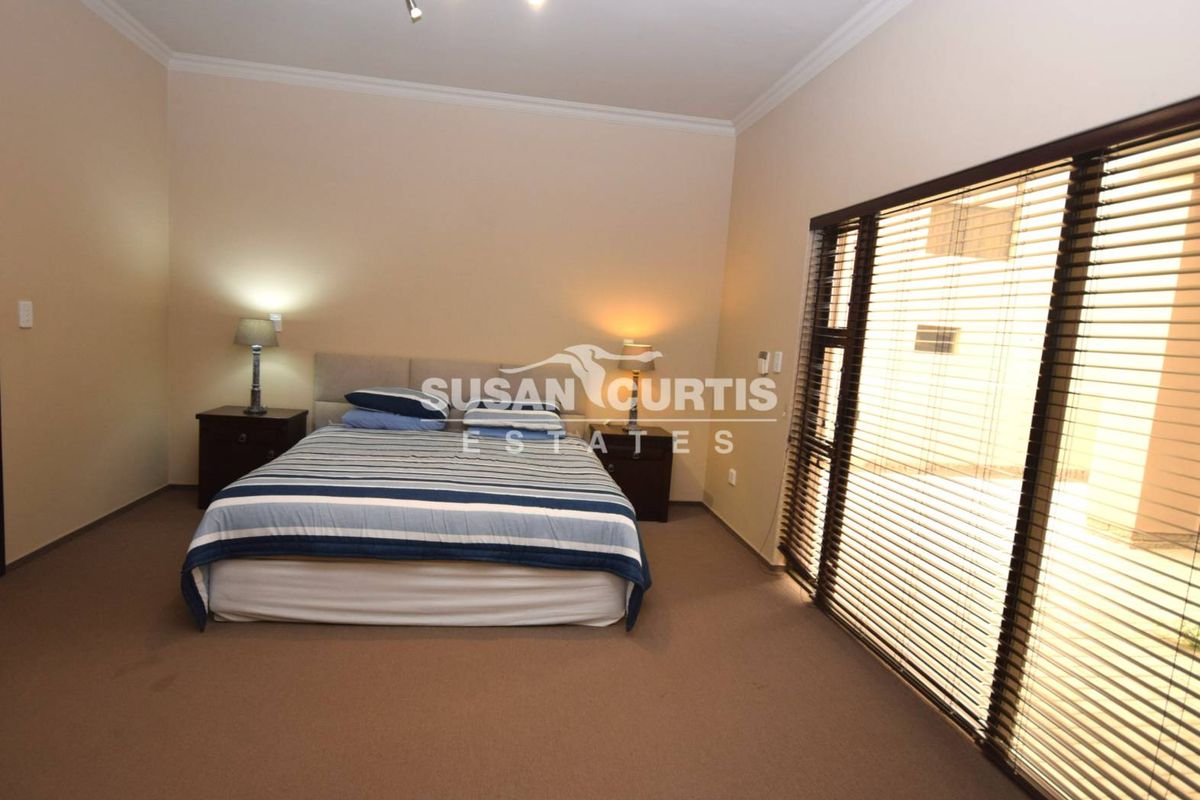 Spacious bedroom featuring neutral wall tones, carpeted flooring, and large sliding glass doors with fitted blinds providing access to the exterior.