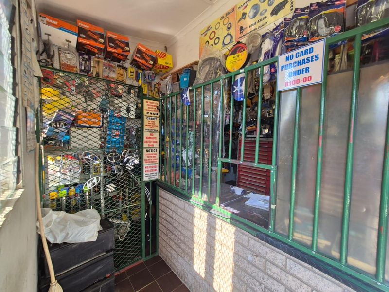 A commercial utility or service counter area featuring security gating, metal bars, and tiled flooring, currently utilized for retail storage.
