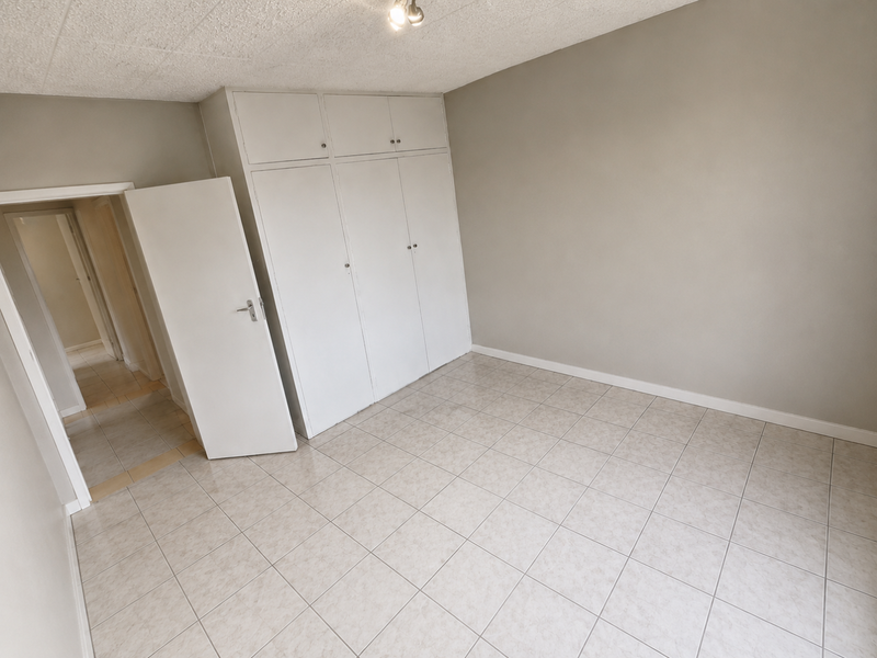 A clean, empty bedroom featuring neutral tiled flooring and ample built-in cupboard storage space.