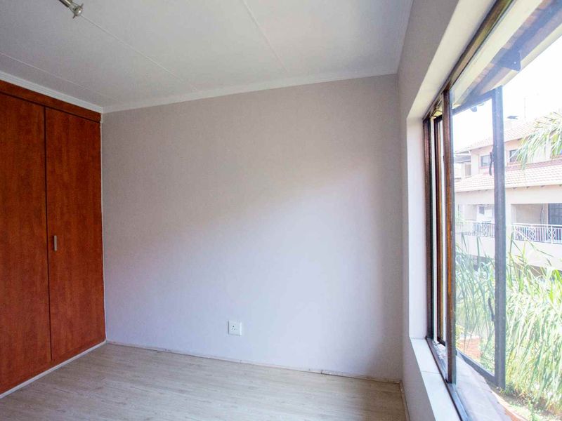 An empty bedroom featuring laminate flooring, a built-in wooden wardrobe, and a large window overlooking the complex exterior.