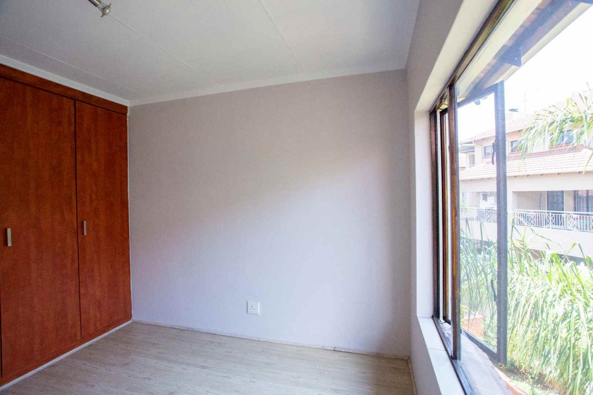 An empty bedroom featuring laminate flooring, a built-in wooden wardrobe, and a large window overlooking the complex exterior.
