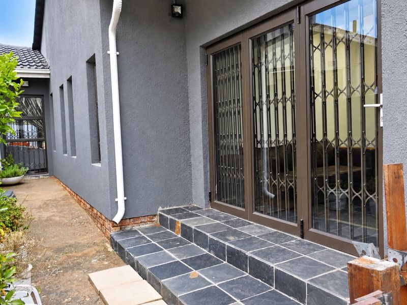 Rear exterior view featuring slate tiled steps leading to aluminium sliding doors with security gates, set against a grey rendered wall.