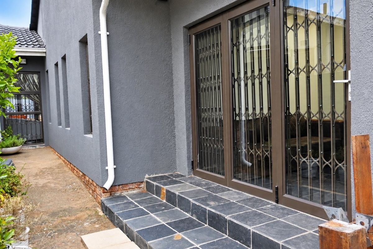 Rear exterior view featuring slate tiled steps leading to aluminium sliding doors with security gates, set against a grey rendered wall.