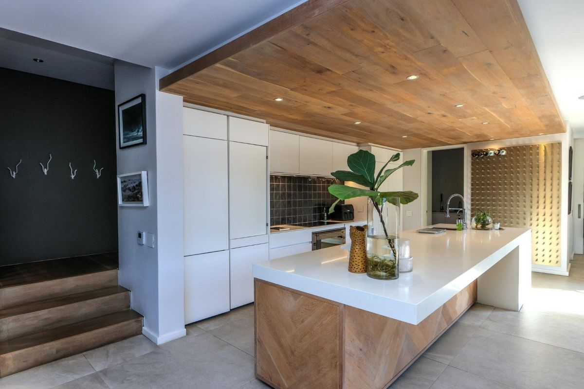 Modern kitchen featuring a large island with stone countertops, integrated cabinetry, a timber-clad ceiling, and high-end finishes throughout.