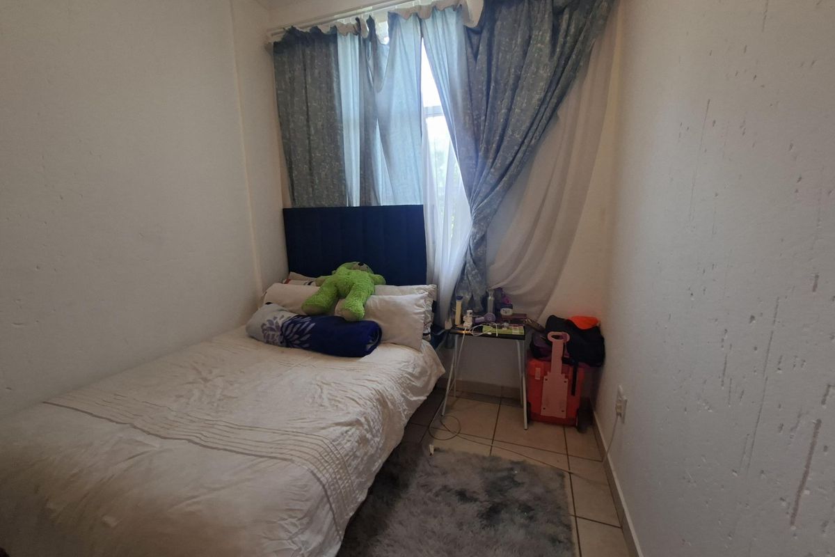 A compact bedroom featuring tiled flooring and a window with curtain fixtures, requiring minor wall repairs and cosmetic updates.