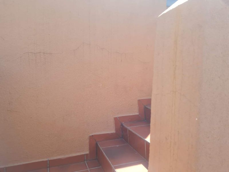 An exterior staircase with tiled steps and a plastered wall showing visible cracks and surface staining.