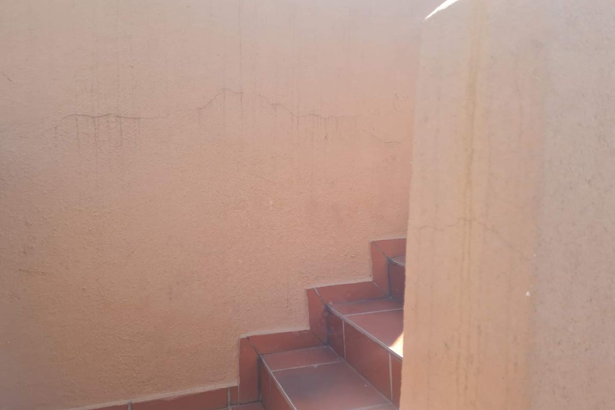 An exterior staircase with tiled steps and a plastered wall showing visible cracks and surface staining.