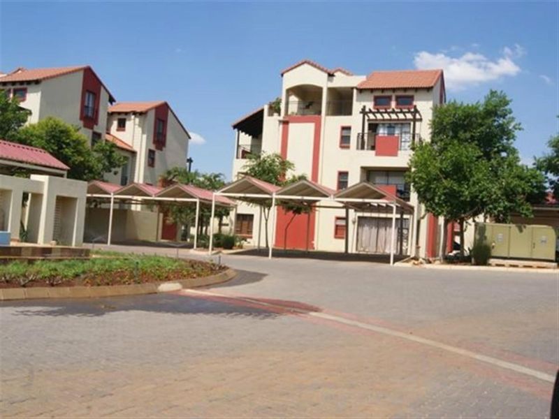 Exterior view of a multi-story apartment complex featuring covered parking bays, paved driveways, and private balconies.