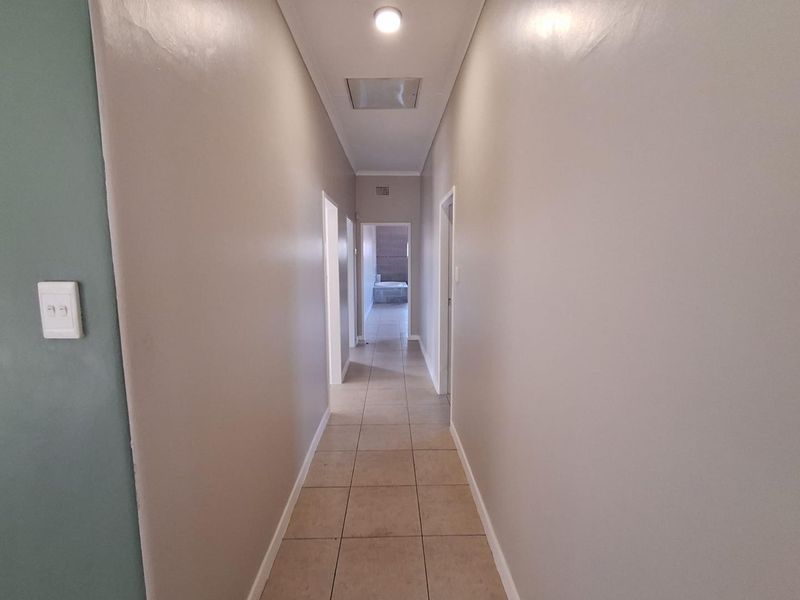 A clean, neutral-toned hallway featuring tiled flooring and a ceiling access hatch, providing access to various rooms within the home.