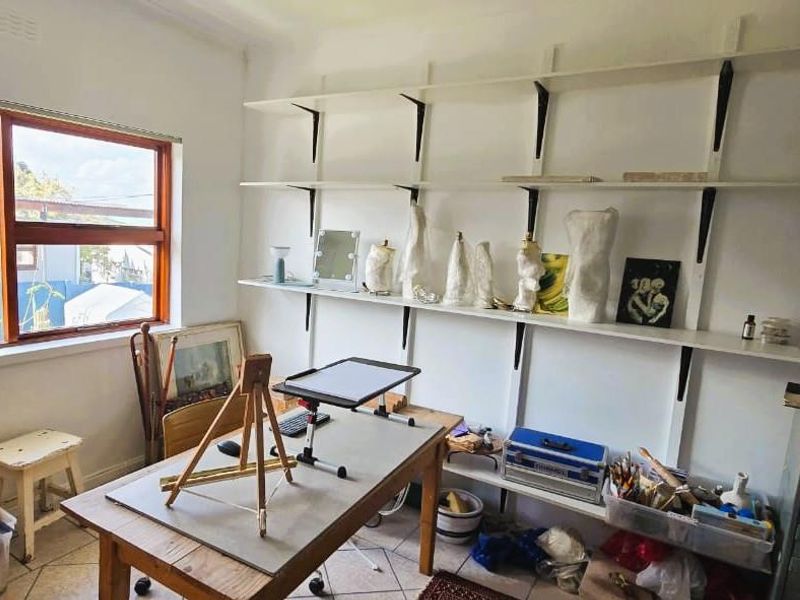 A functional home office space featuring tiled flooring, timber-framed windows, and extensive built-in wall shelving for storage.