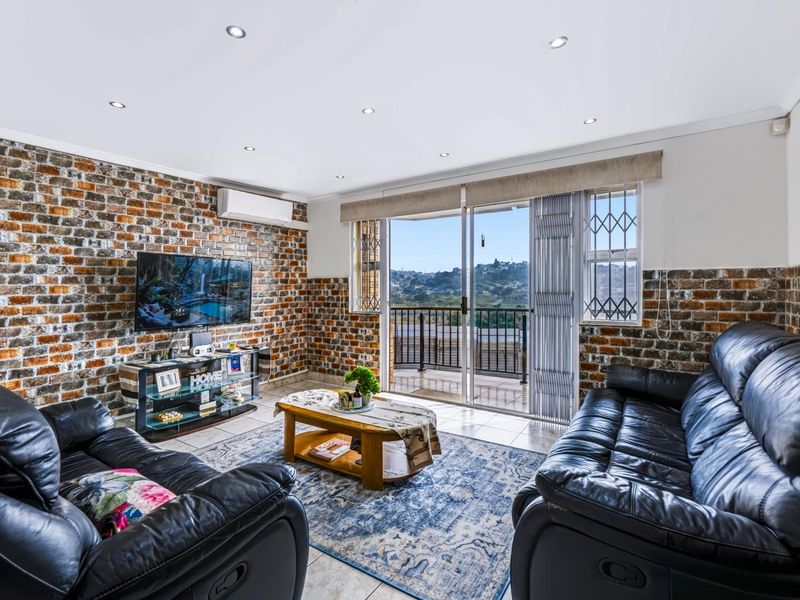 Spacious living room featuring an exposed brick wall, recessed lighting, and a sliding glass door leading to a balcony with scenic views.