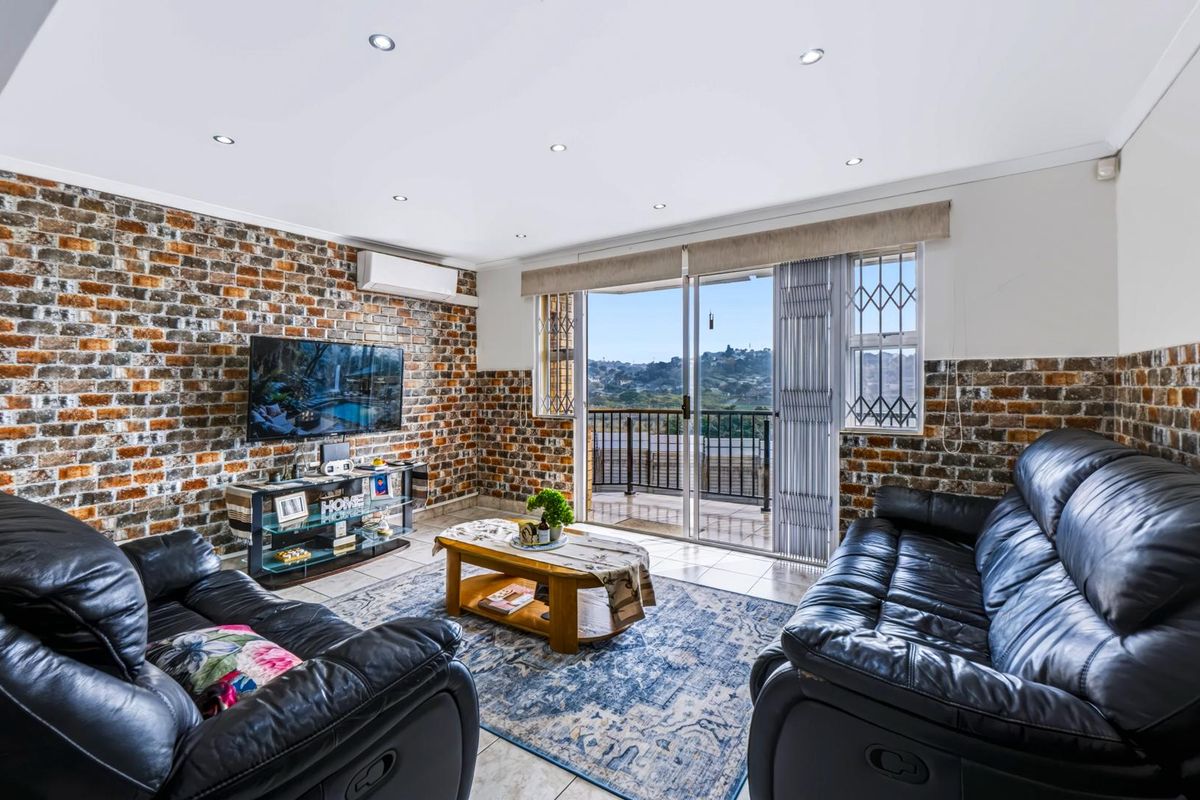 Spacious living room featuring an exposed brick wall, recessed lighting, and a sliding glass door leading to a balcony with scenic views.