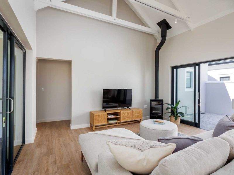 Bright living room featuring a vaulted ceiling with exposed trusses, a modern freestanding fireplace, and large sliding glass doors leading to an outdoor area.
