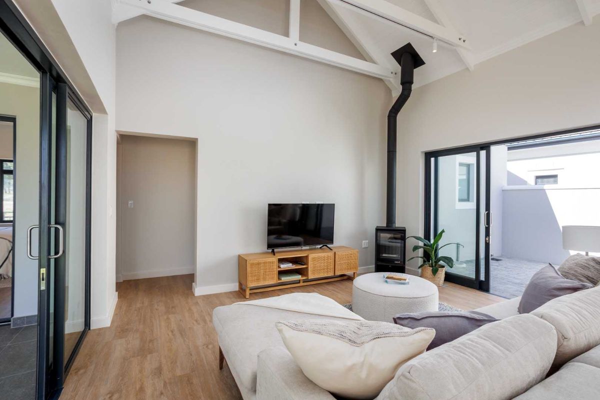 Bright living room featuring a vaulted ceiling with exposed trusses, a modern freestanding fireplace, and large sliding glass doors leading to an outdoor area.