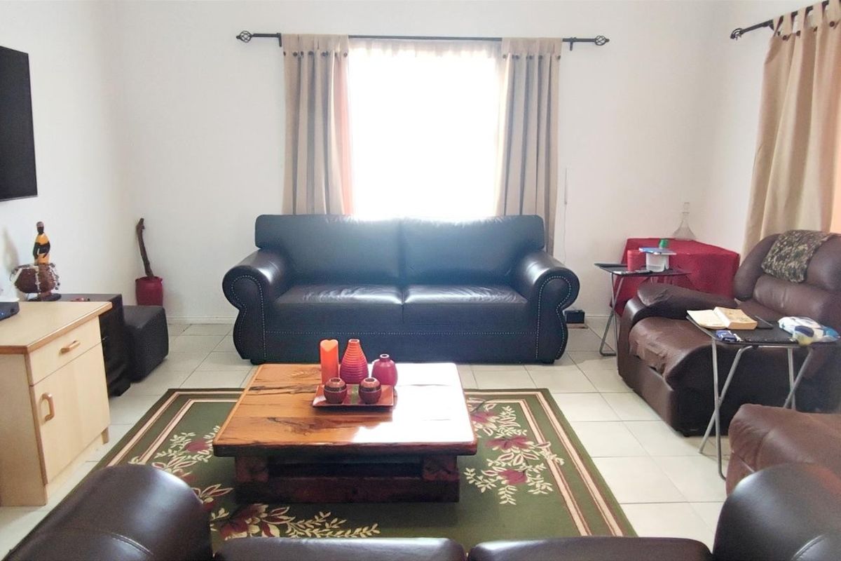 A comfortable living room featuring tiled flooring and large windows with curtain rods, providing a functional and well-lit space for relaxation.