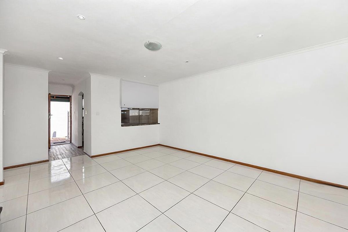 A bright, empty living area featuring neutral tiled flooring, recessed downlighting, and a convenient pass-through window connecting to the adjacent space.